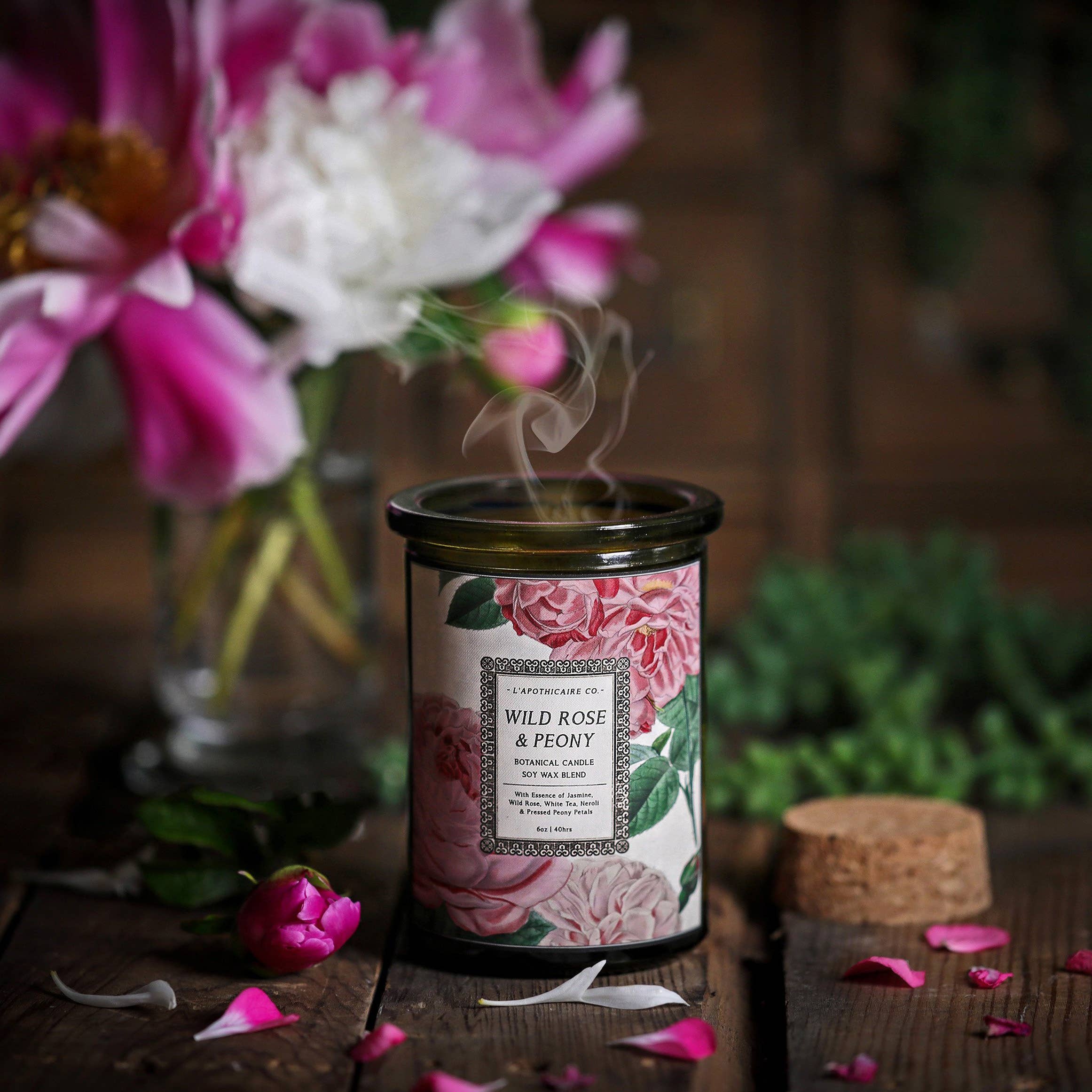 Candle in green glass jar with cork lid.  Label has illustrations of o=pink roses and peonies. Label states fragrance as "Wild Rose and Peony"