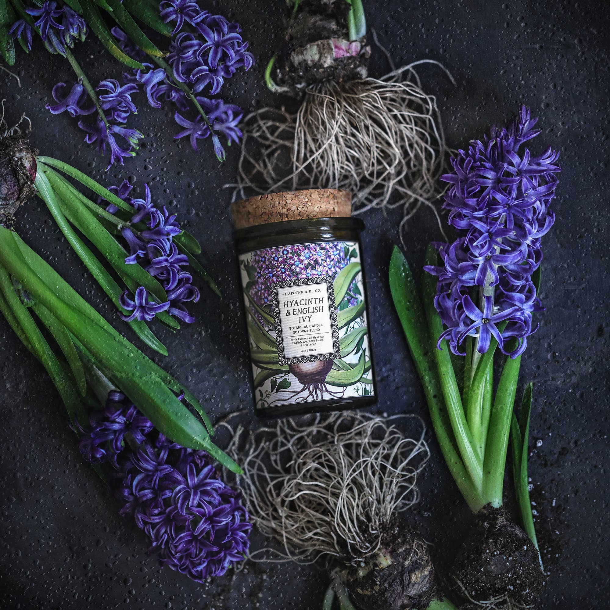 Candle in green glass jar with cork lid, label with illustrations of hyacinth flower, bulb and ivy.  Label states the scent " Hyacinth and English Ivy"