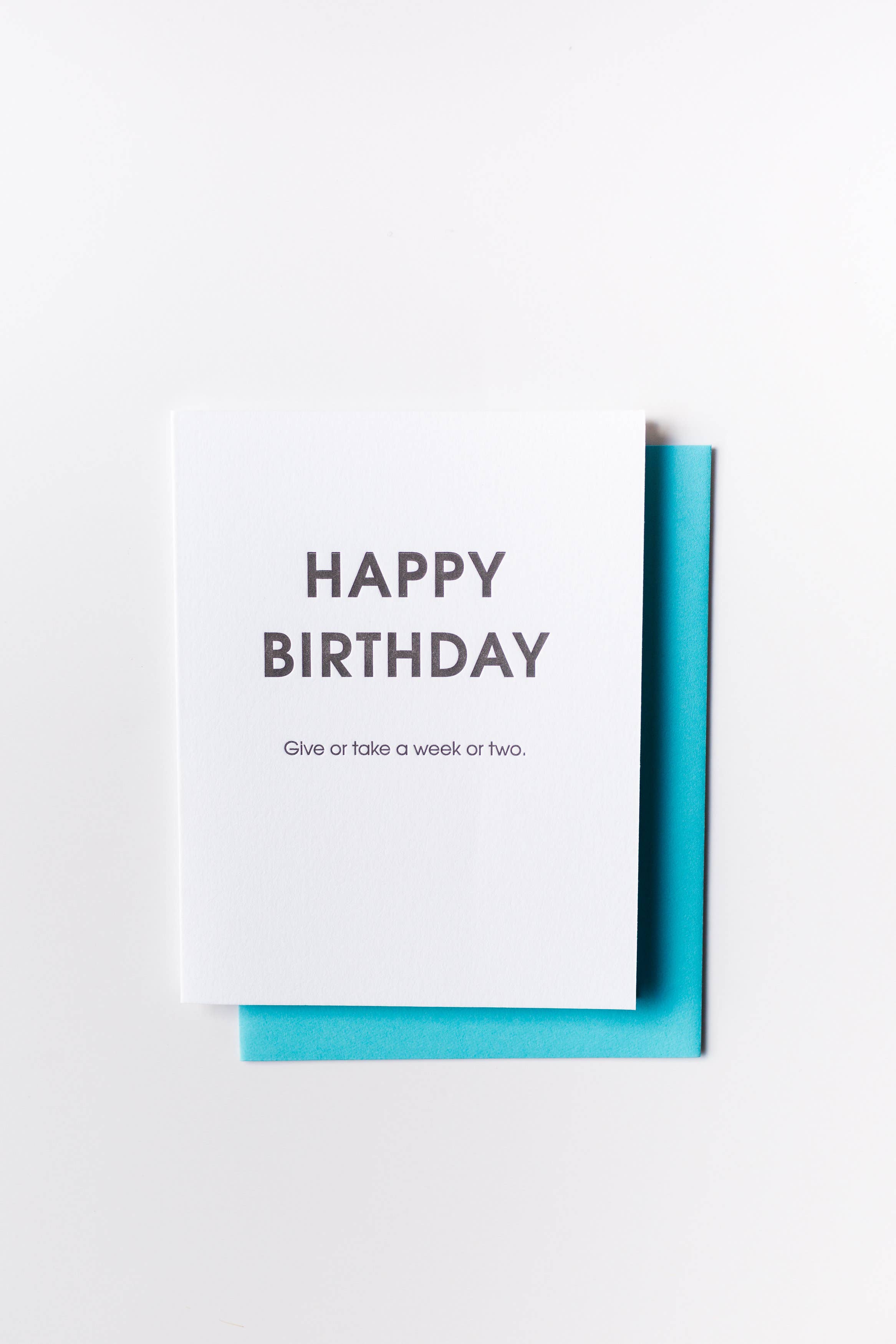 White card with " Happy birthday give or take a week or two" in black lettering.  Fluorescent blue envelope.