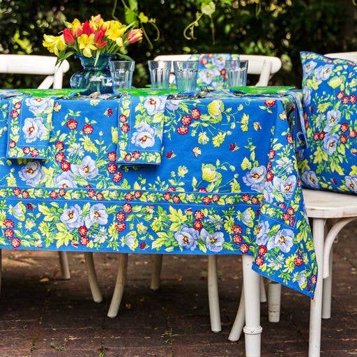 Blue cotton tablecloth with red, yellow and white flowers, and green foliage.