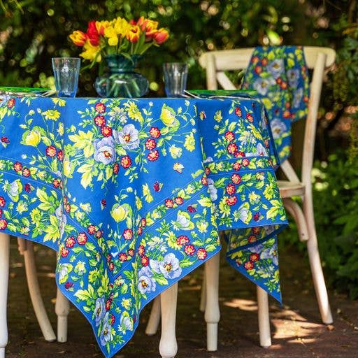 Blue cotton tablecloth with red, yellow and white flowers, and green foliage.