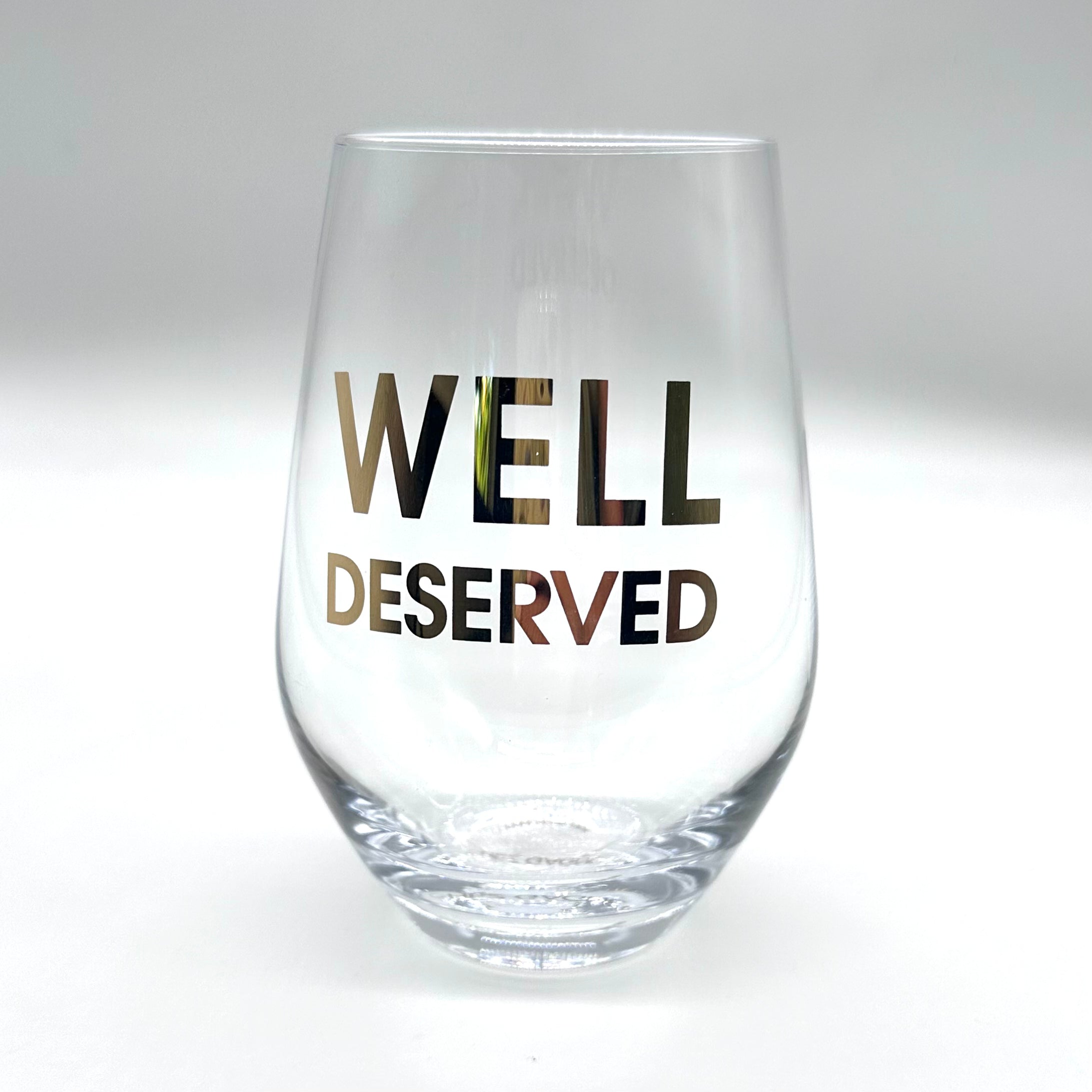 Clear wine glass with "WELL DESERVED" in gold lettering.