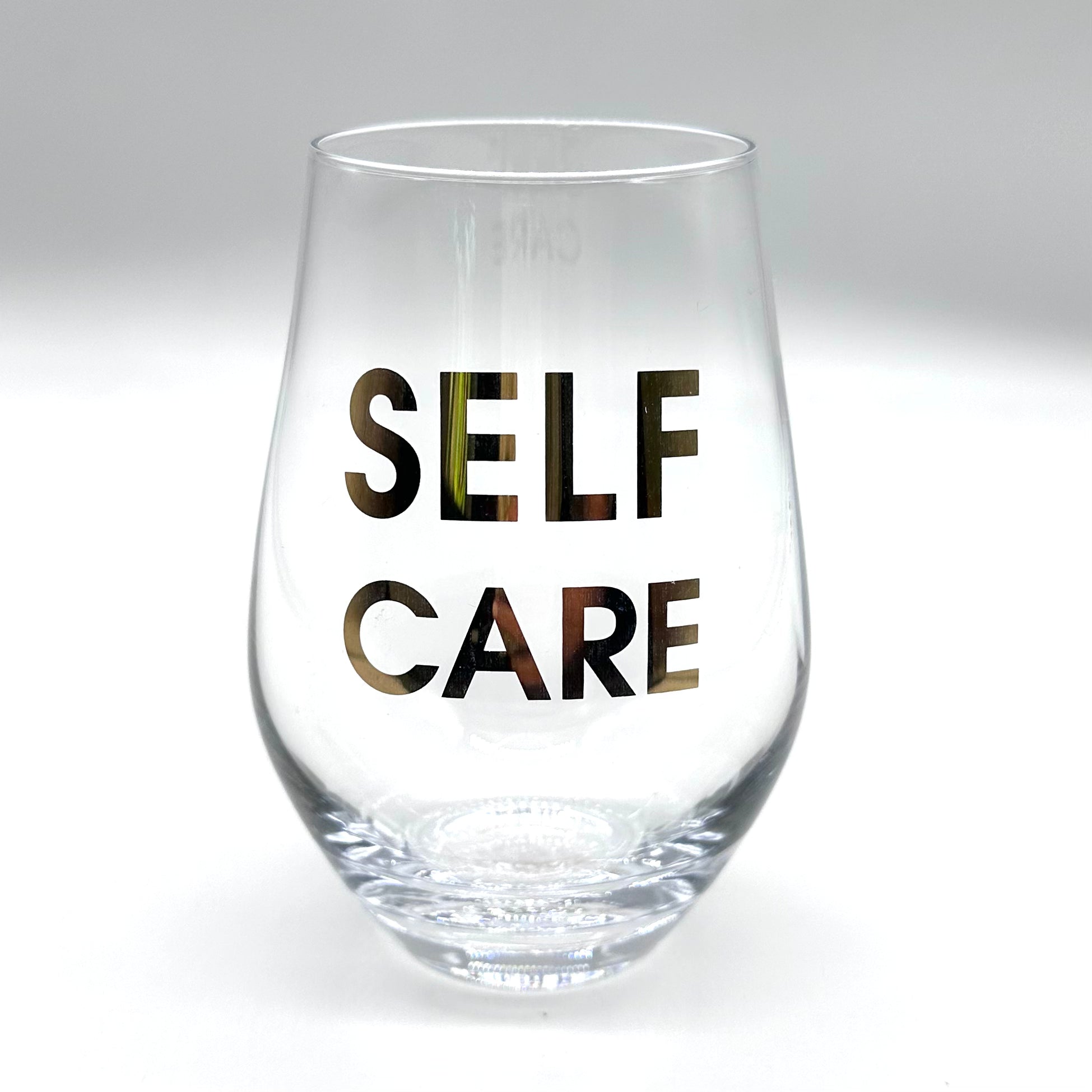 Clear wine glass with "SELF CARE" in gold lettering.