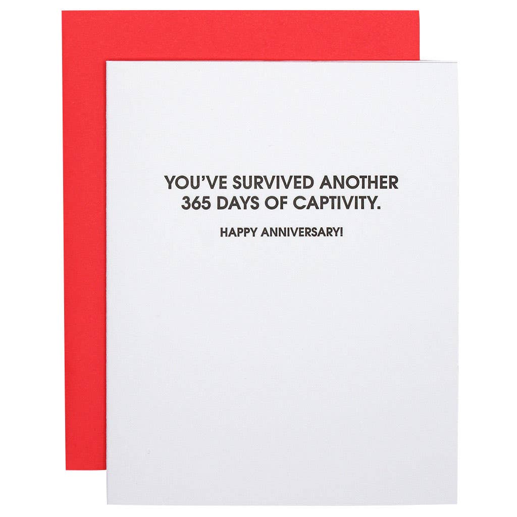 White card with black text stating "you've survived another 365 days of captivity. happy anniversary!".  Neon red envelope.