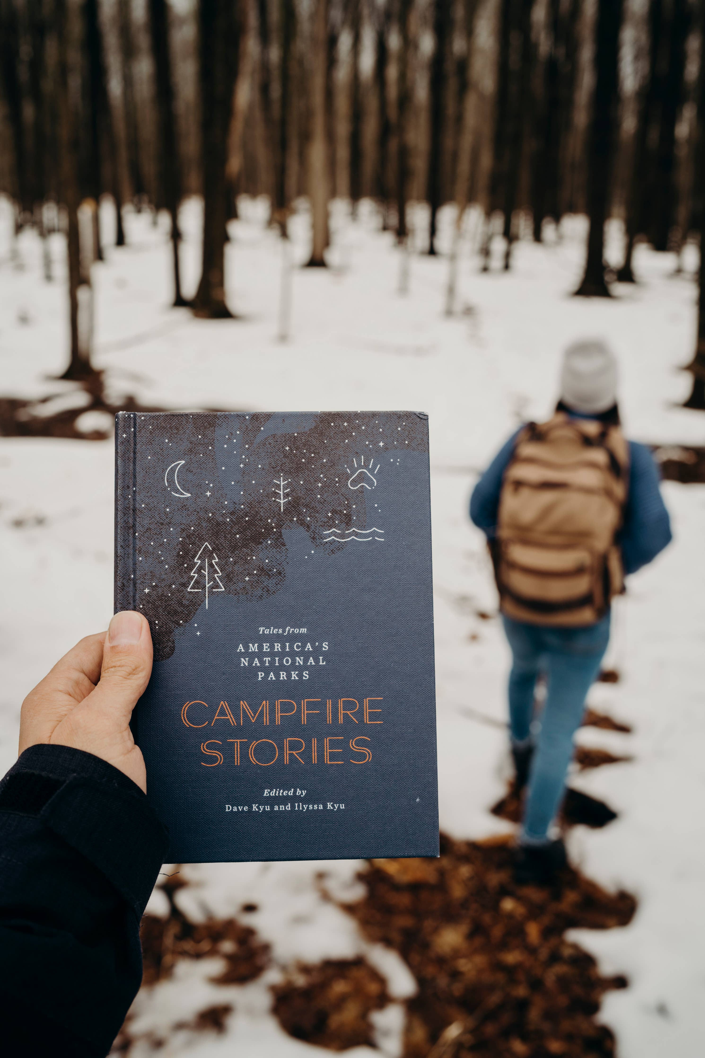 Person holding "Campfire Stories" out in snow, walking.