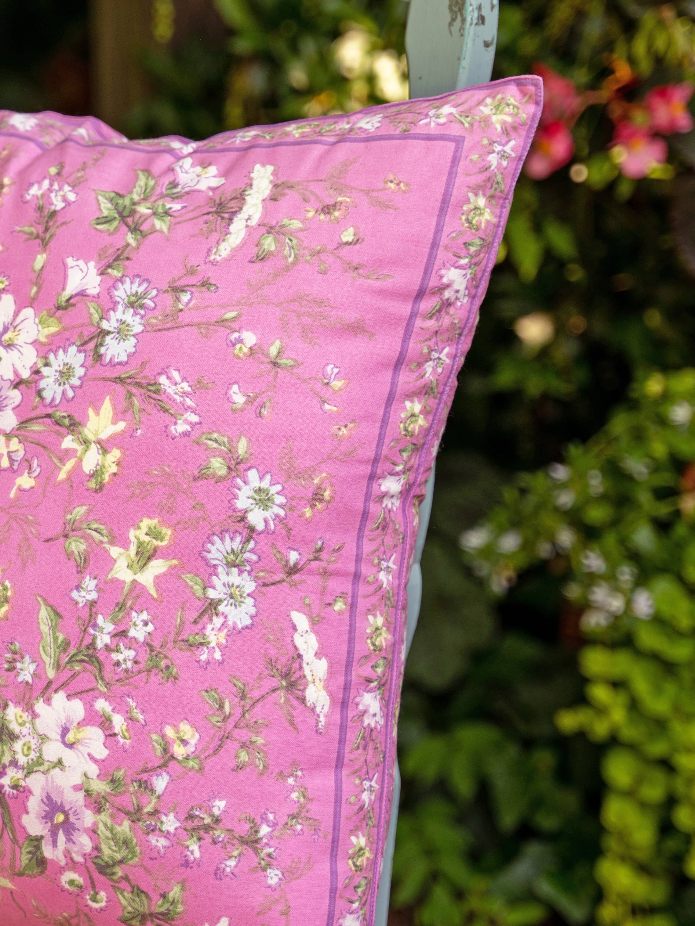 Pillow with cotton fabric, pink background with white and pink flowers and green foliage.