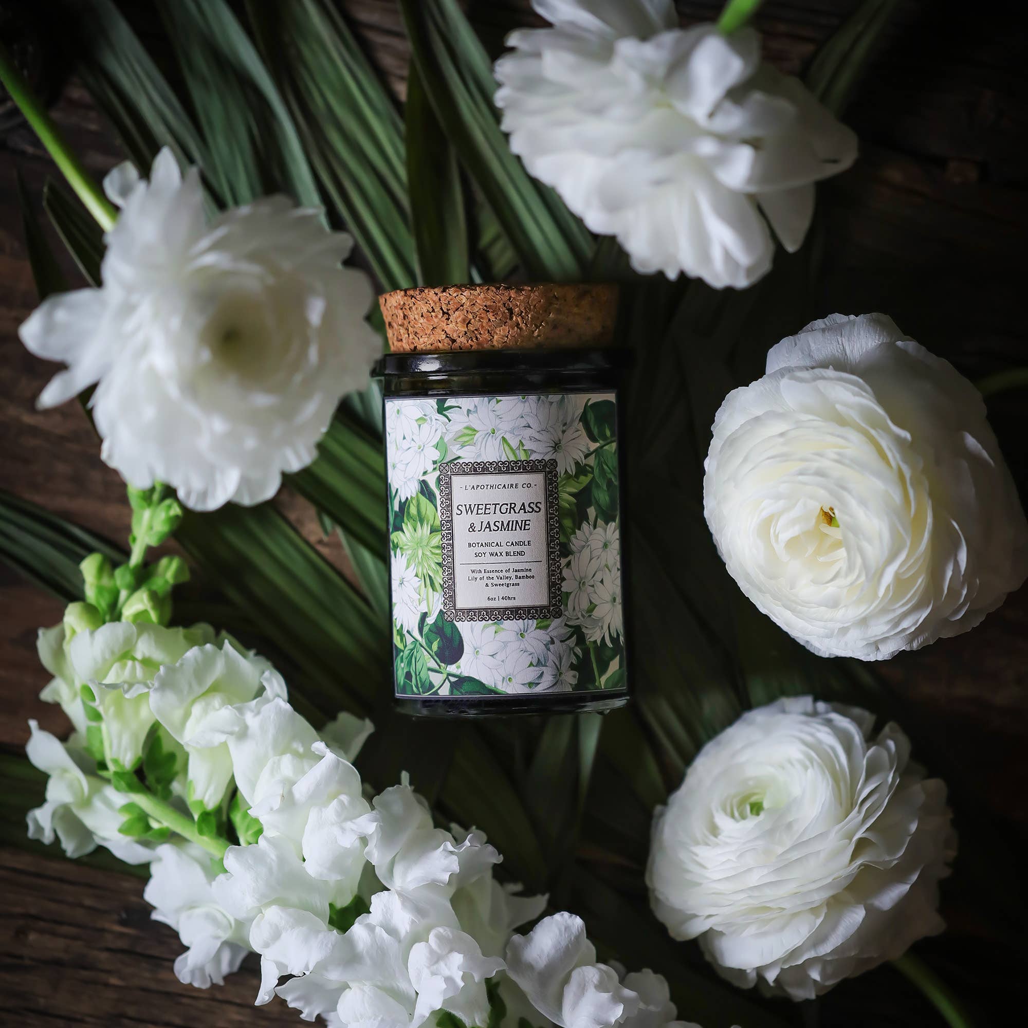 Candle inside green glass jar with cork lid, white jasmine flowers with green leaves on label.  Label states "sweetgrass and jasmine" as the scent. 