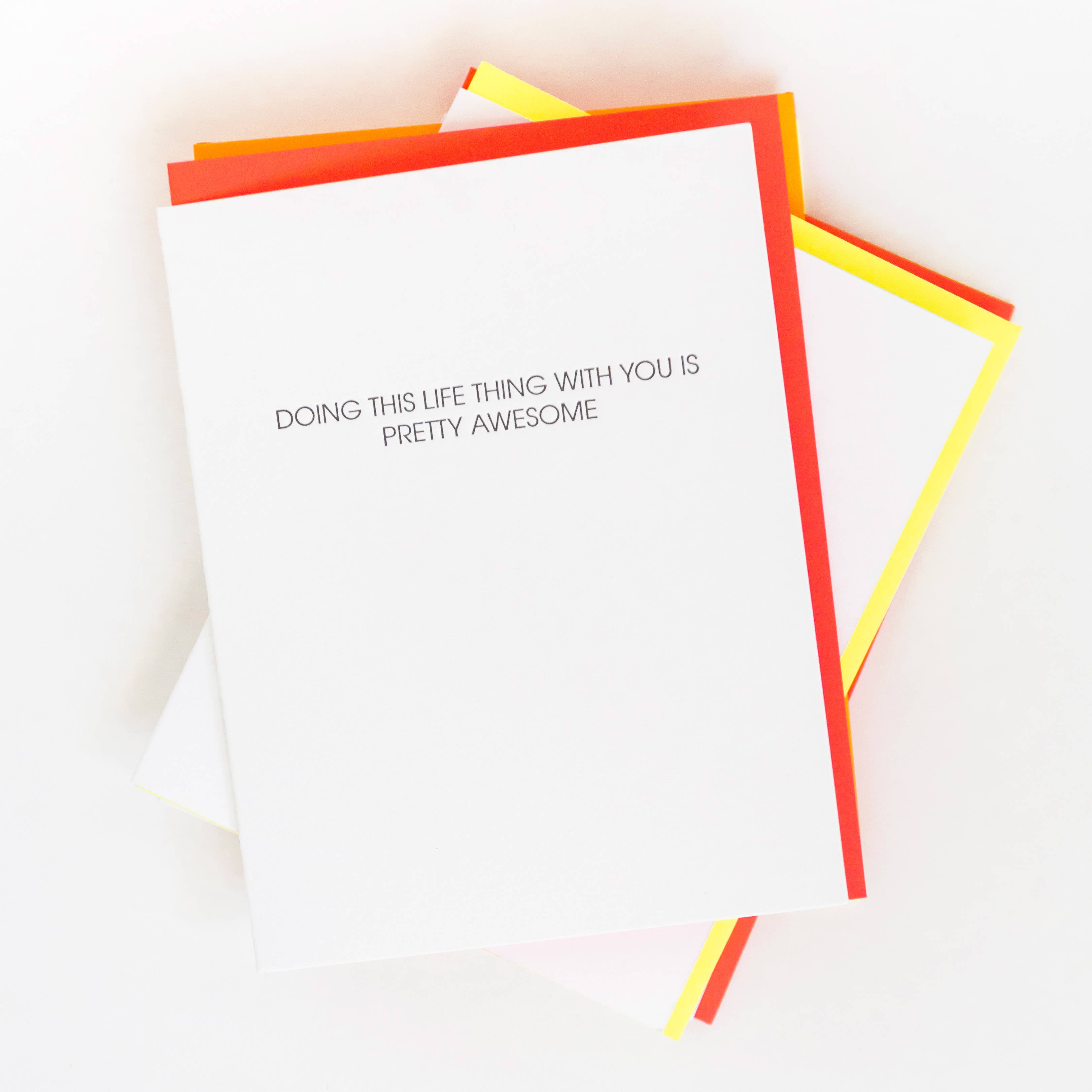 White card with "Doing this life thing with you is pretty awesome" in black lettering. Neon red envelope.