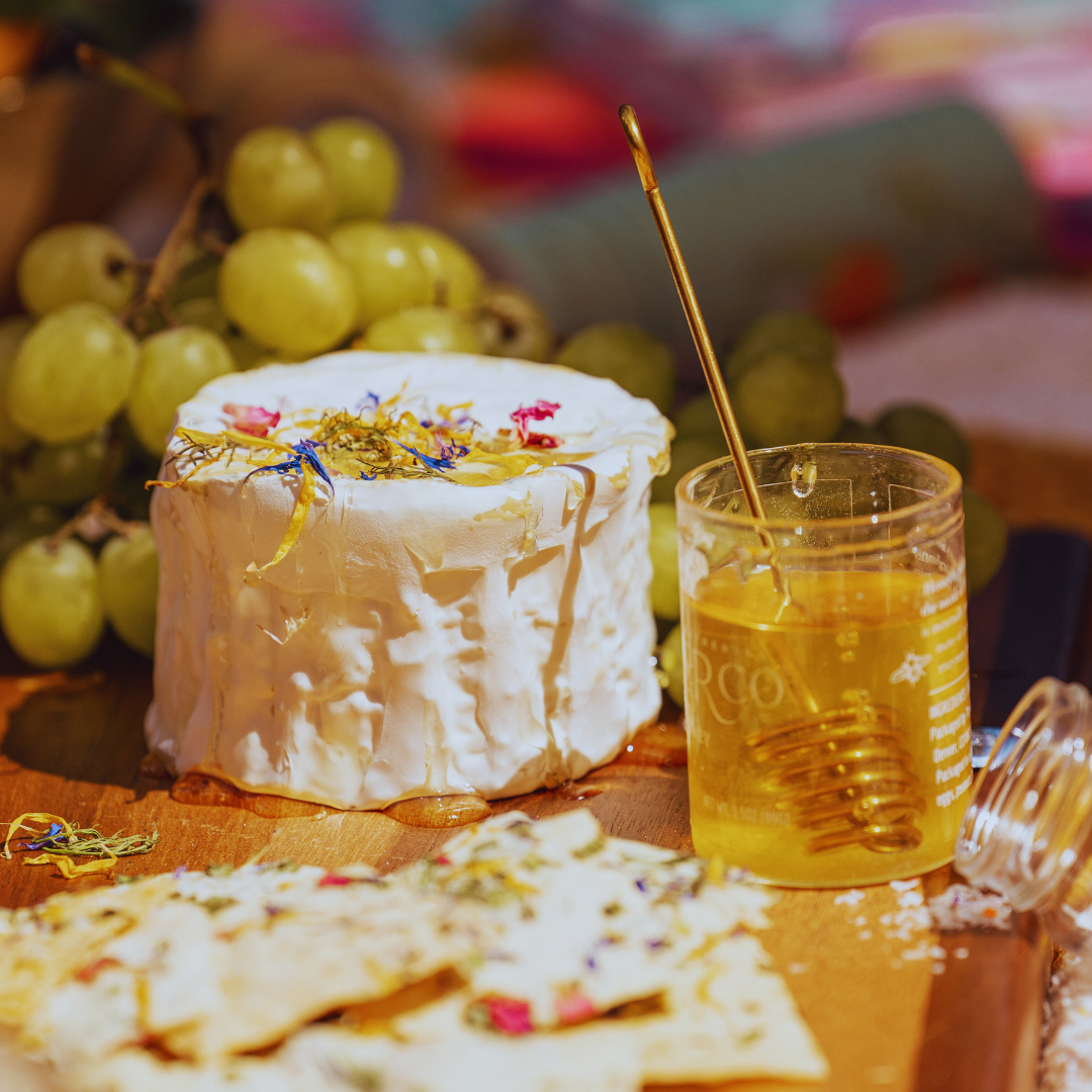 Wheel of cheese with edible flowers on top and jar of hone on charcuterie board