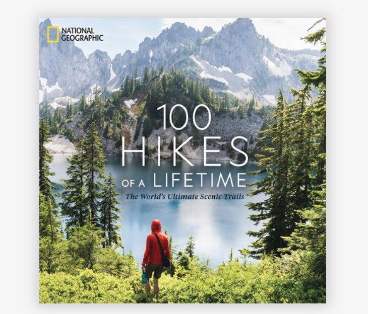 Pictured is a book of a mountain scene with a lake and a hiker the title of the book is 100 hikes of a lifetime the world's ultimate scenic trails book by National Geographic and Kate Siber.