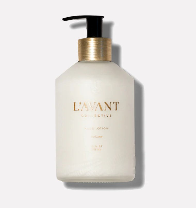 White glass container with gold and black pump top.  Gold lettering states "L'avant Collective Hand Lotion Fresh Linen"